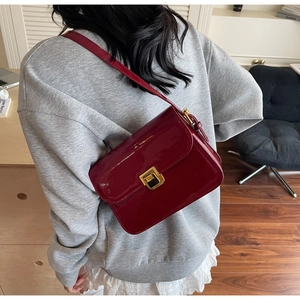 Detail of burgundy patent leather shoulder bag with glossy finish and gold square buckle