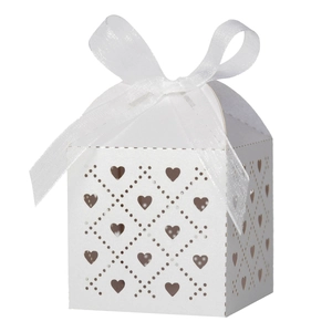 Detail of white laser-cut wedding favor box with hollow heart patterns and ribbon