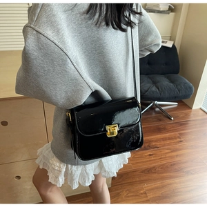 Detail of black patent leather crossbody bag with elegant gold metal square buckle