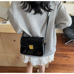 Close-up of a black patent leather shoulder bag with a shiny finish and gold buckle