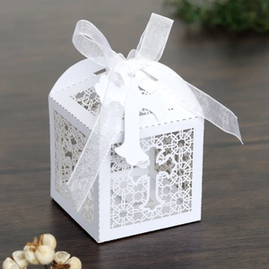 Detail of white laser-cut cross candy box with intricate floral patterns and silk ribbon