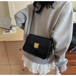 Detail of black patent leather crossbody bag with polished gold square twist lock clasp