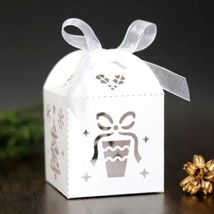 Close-up of white laser-cut Christmas gift box with elegant tree patterns and ribbon