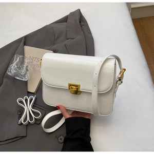 Close-up of white patent leather crossbody bag with golden rectangular turn-lock buckle