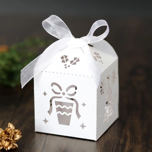 Detail of white laser-cut Christmas house gift box with ribbon on wooden background