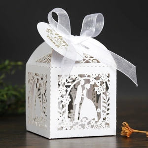 Detail of white laser-cut wedding favor box with ribbon and heart-shaped thank you tag