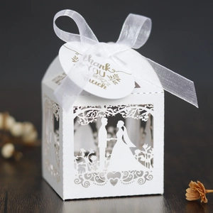Close-up of white laser-cut wedding favor box with ribbon and gold Thank You tag