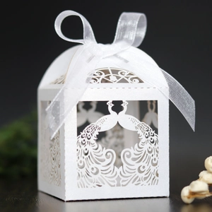 White laser-cut peacock wedding candy box with elegant silk ribbon bow on wood surface