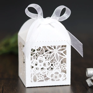 Macro view of white laser-cut hollow candy box with floral patterns and organza ribbon