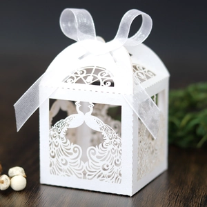 Detail of white laser-cut peacock wedding favor box with a delicate ribbon bow on wood
