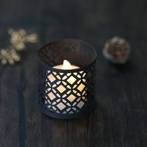 Detail of black geometric hollow candle holder with warm yellow LED tea light on wood