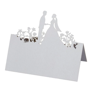 Macro shot of white laser-cut wedding place card with bride and groom silhouette