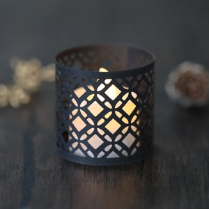 Close-up of black laser-cut geometric hollow candle holder with warm yellow light