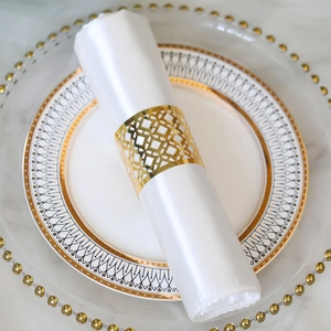 Close-up of golden geometric hollow napkin ring on white satin napkin on marble table