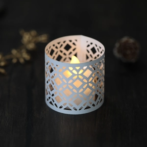 Detail of laser-cut geometric candle holder with warm yellow LED tea light on wood