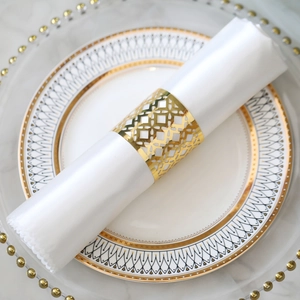 Close-up of golden hollowed-out napkin ring with white satin cloth on elegant tableware