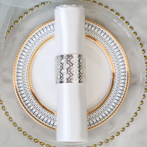 Close-up of hollow geometric silver napkin ring on a white silk napkin and elegant plate