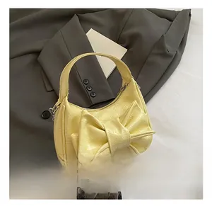 Détail du sac croissant jaune clair avec texture froissée et nœud sur un blazer gris