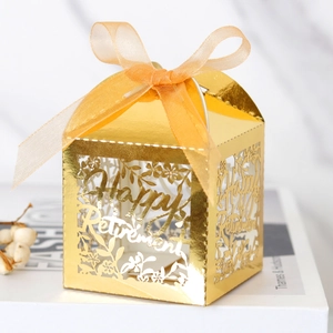 Gros plan sur une boîte cadeau dorée Happy Retirement ajourée au laser avec ruban orange