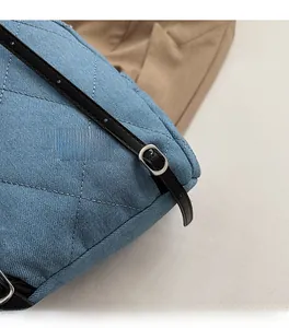Detail of blue denim quilted tote with silver buckle and black leather shoulder strap