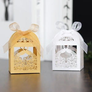 Detail view of laser-cut peacock candy boxes in gold and white with satin ribbons