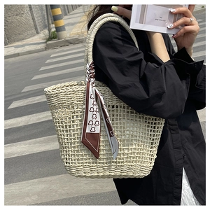 Detail of hollow woven straw tote bag featuring decorative geometric print silk scarf