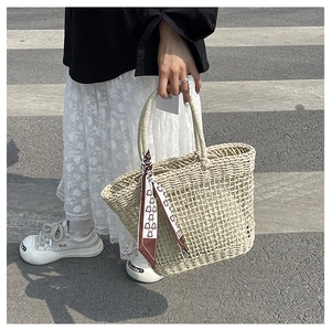 Detail of oat straw woven tote bag with hollow knit pattern and decorative silk scarf