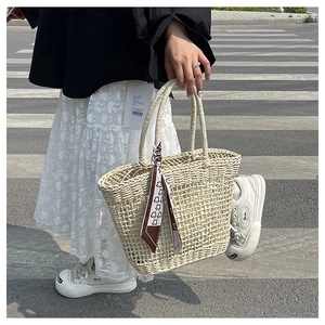 Detailed close-up of woven straw tote bag with decorative printed silk scarf on handle