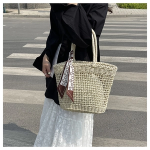 Detail of hollow woven straw tote bag featuring a decorative bear print silk scarf handle