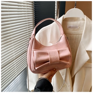 Gros plan d'un sac hobo rose en forme de croissant avec grand nœud et bandoulière chaîne
