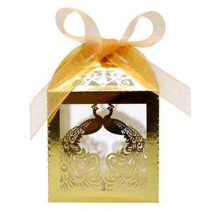 Close-up of golden laser-cut peacock wedding candy box with elegant champagne ribbon