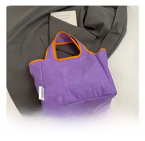Detail of purple canvas tote bag with orange contrast trim and white brand label