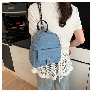 Detail of blue denim quilted mini backpack featuring metal chain straps and turn-lock closure