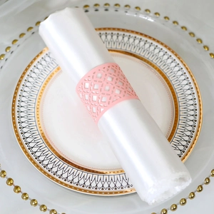 Macro view of pink laser-cut paper napkin ring with geometric hollow pattern on a white napkin