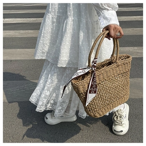 Detail of hand-woven brown straw tote bag decorated with a silk scarf on the street