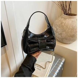 Détail du sac croissant en cuir verni noir avec un grand nœud et une bandoulière chaîne