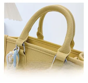 Detail view of yellow litchi leather handbag with silver hardware and colorful charm