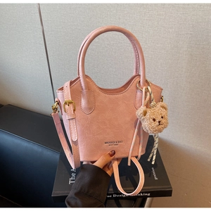 Dettaglio borsa a secchiello rosa con trama plissettata e ciondolo orsetto di peluche