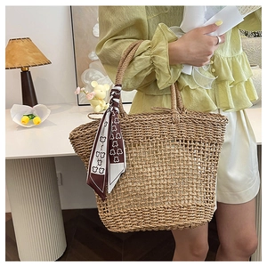 Detail view of woven straw tote bag featuring decorative teddy bear pattern silk scarf handle