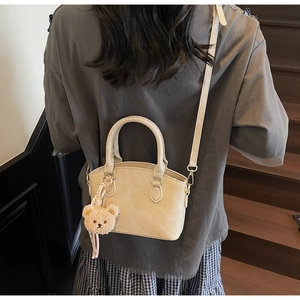 Detail of beige crocodile embossed bucket bag with plush bear charm on model