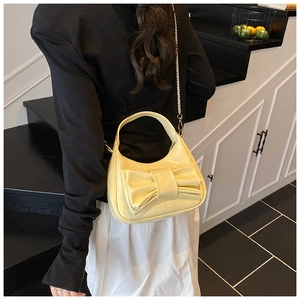 Détail d'un sac demi-lune jaune crème avec un grand nœud et une bandoulière en chaîne