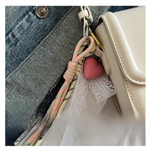 Detailed close-up of woven pink and yellow lanyard with heart charm on litchi leather bag