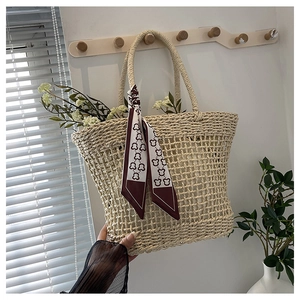 Close-up of woven straw tote bag featuring a decorative dark red patterned silk scarf