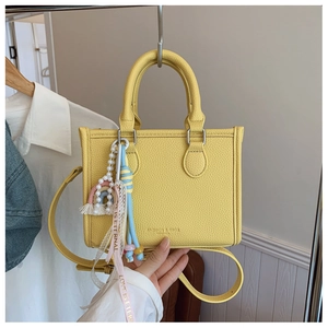 Detail of yellow lychee leather tote bag with rainbow charm and pearl ribbon handle