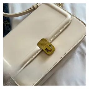 Close-up of matte gold twist lock and fine stitching on cream leather crossbody bag