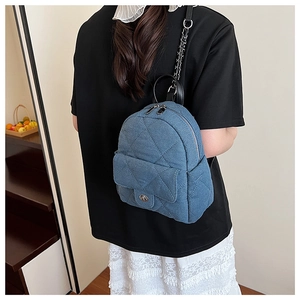 Detail of blue denim quilted mini backpack with silver metal chain straps on model