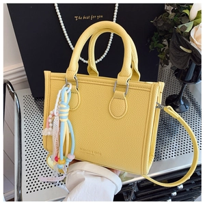 Detail of yellow lychee leather tote bag with woven colorful charms on metal surface