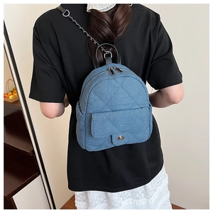 Blue denim quilted backpack with chain straps shown on model in a stylish interior