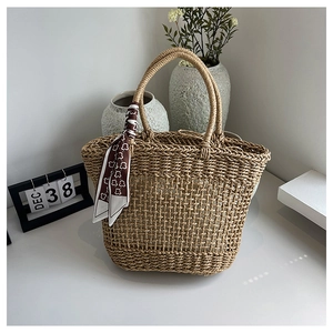 Detail of woven straw tote bag featuring cylindrical handles and decorative floral silk scarf
