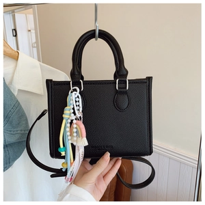 Detail of black lychee grain leather tote with double handles and tassel charm